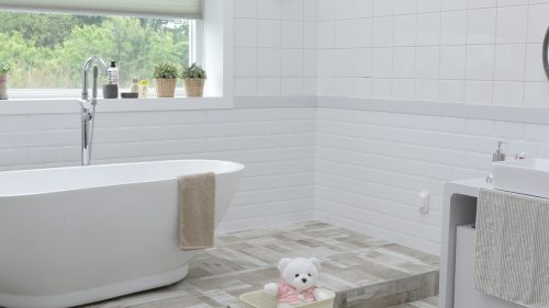 salle de bain avec baignoire dans les tons clairs avec ourson en peluche par terre et plantes à la fenêtre